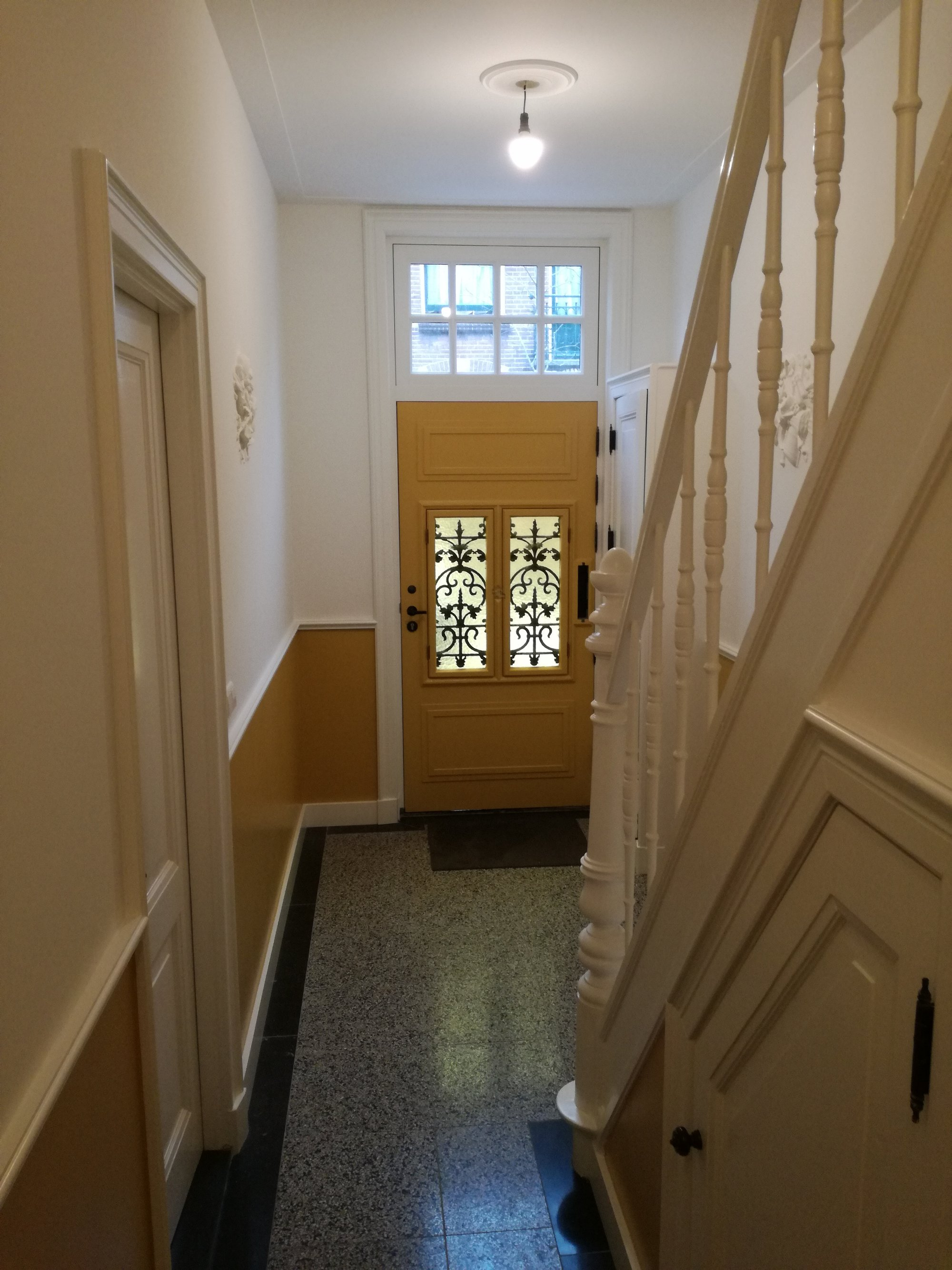 Hal met gele voordeur en witte trap